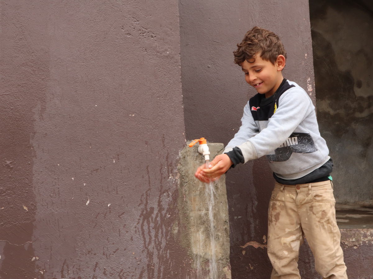 A Syrian boy joyfully washes his hands at a pin-installed tap in his home.