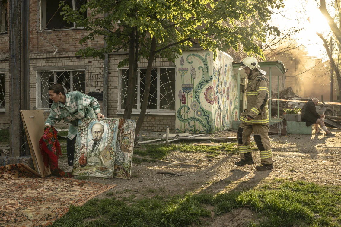 A woman carries portraits of Taras Shevchenko and other Ukrainian cultural figures from a damaged building. 