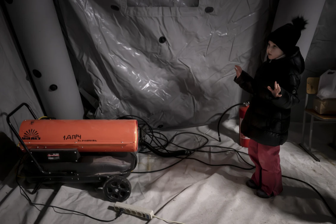 A child stands in front of a heating cannon at an invincibility point, trying to warm up as temperatures reach minus 15 degrees Celsius and large parts of the city remain without heating