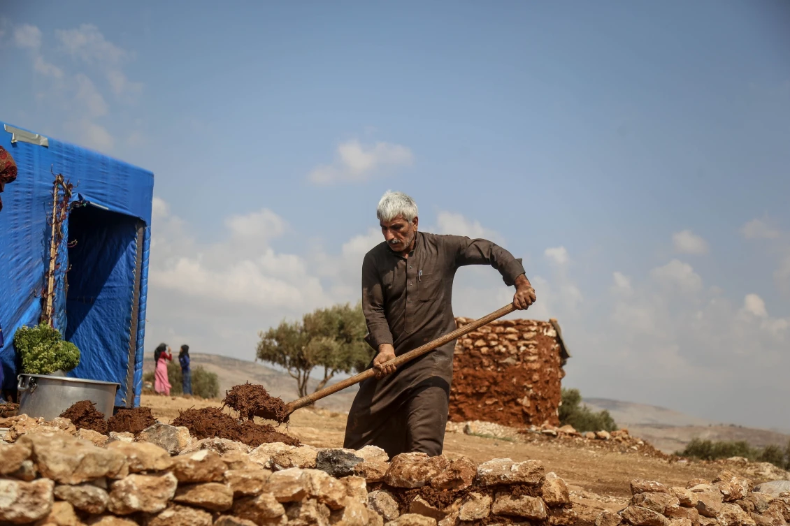An elderly man levelling the ground before erecting a tent for his family.